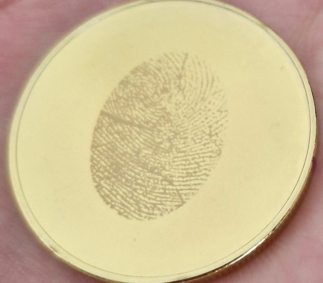 Gold coin with a fingerprint engraving held between fingers
